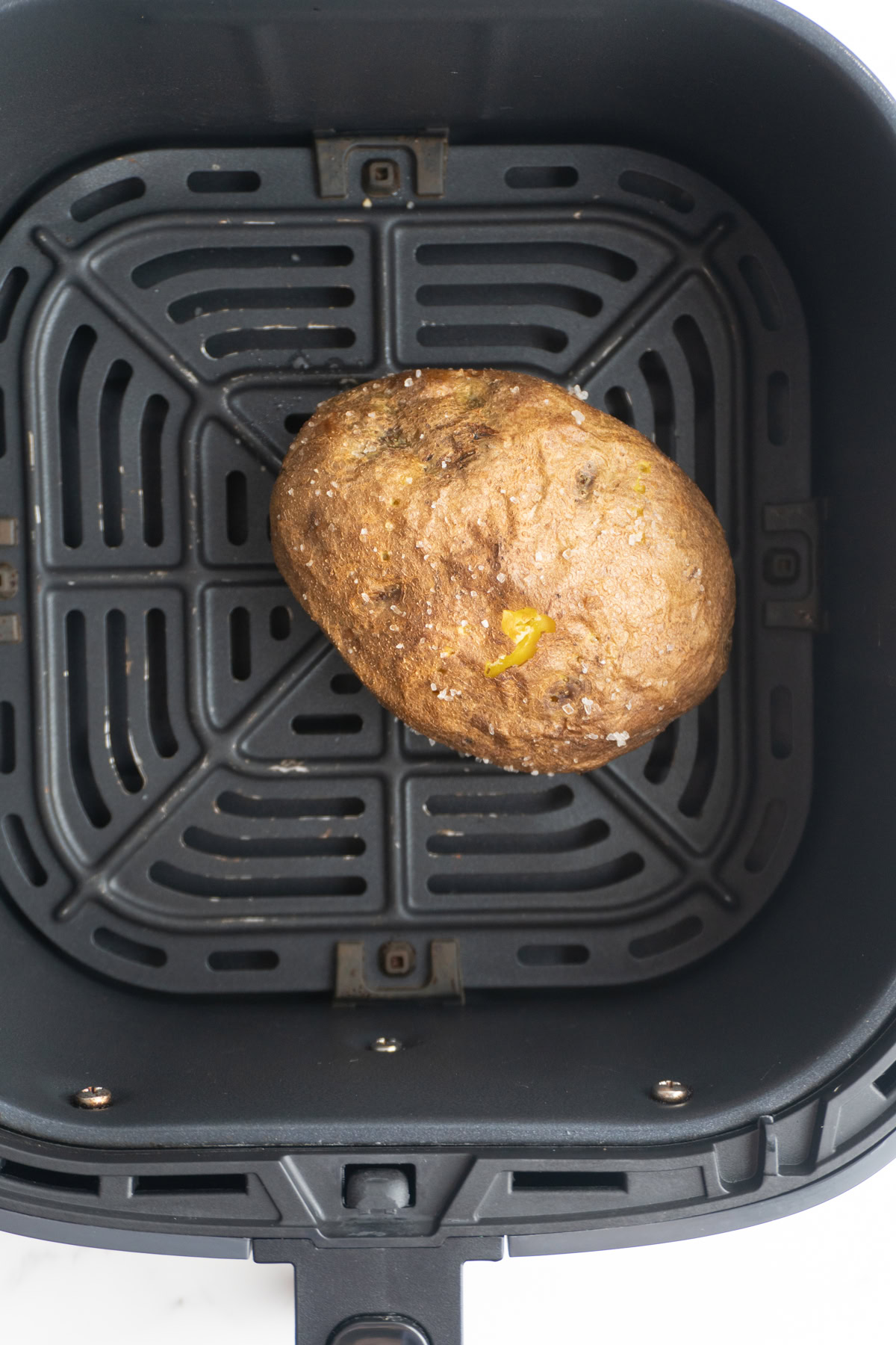 Baked potato finished cooking in the air fryer basket.