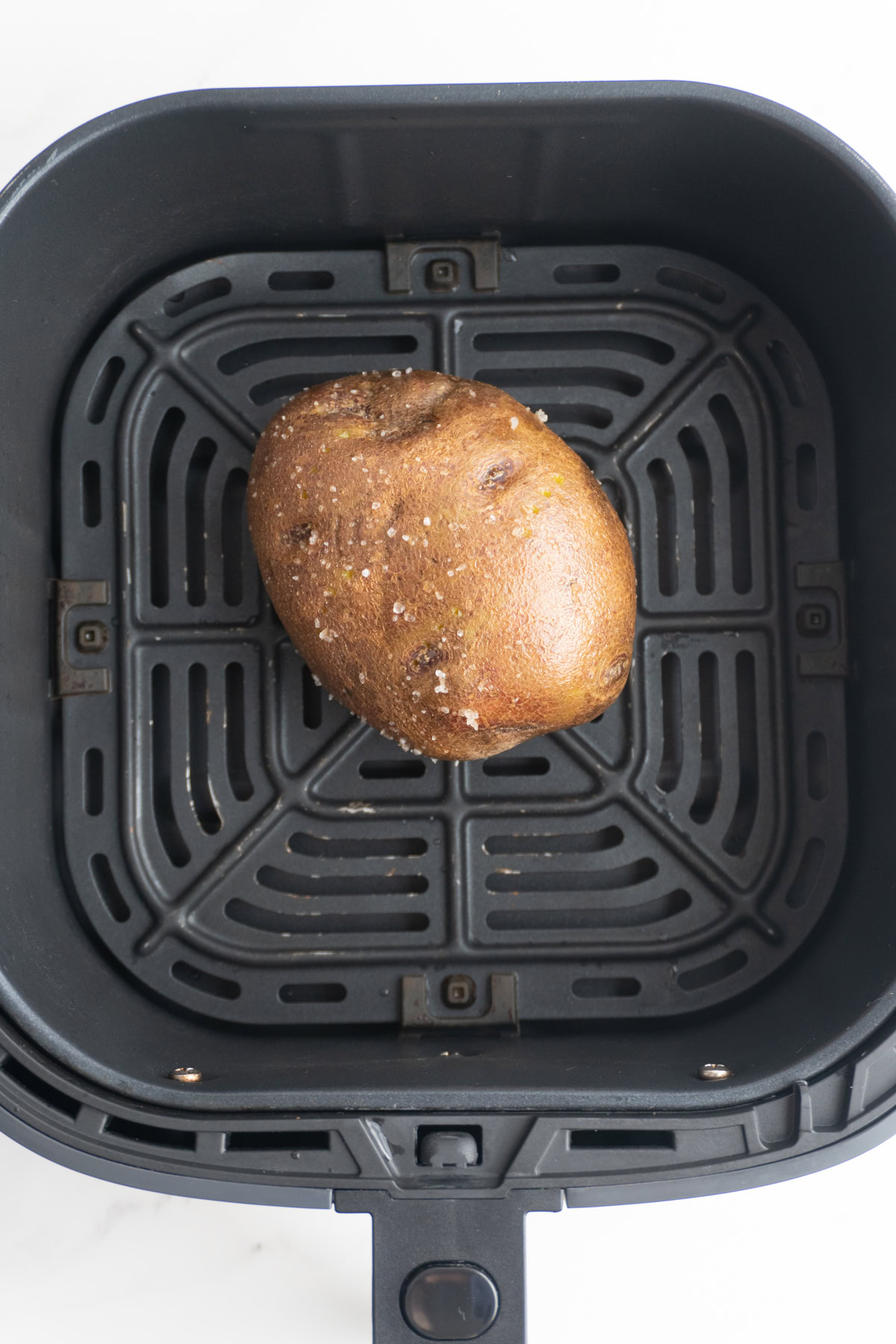 Potato seasoned with salt in an air fryer basket.