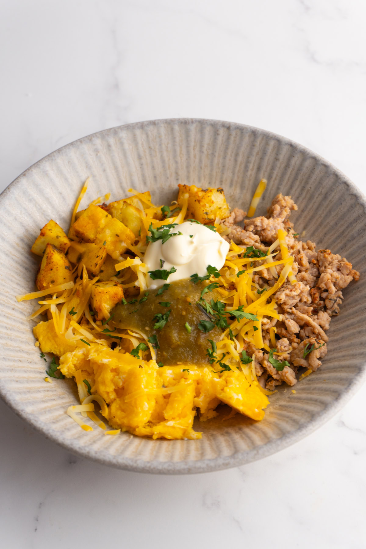 Side view of a breakfast burrito bowl topped with cheese, sour cream, and salsa.