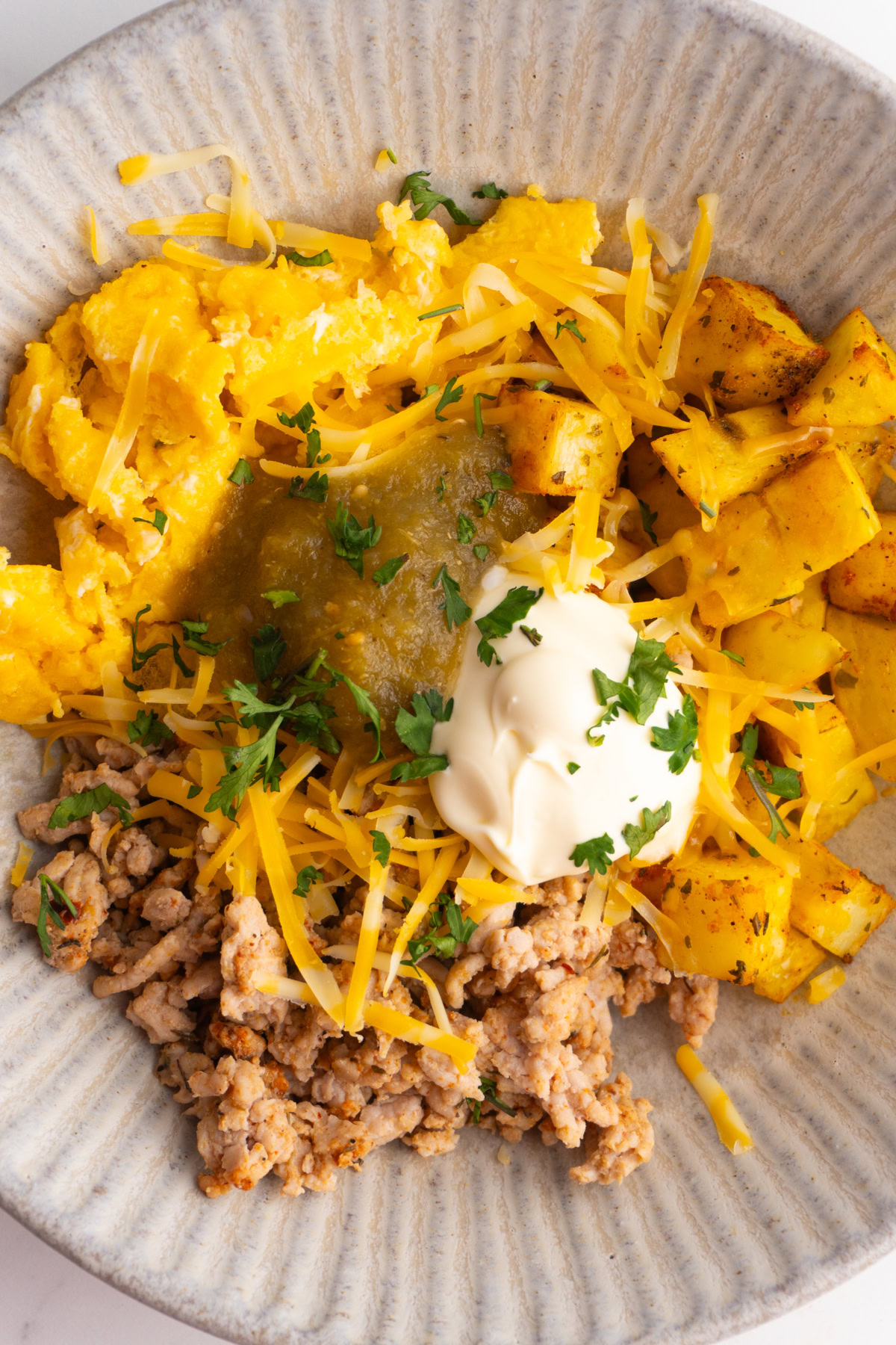 Overhead shot of a breakfast burrito bowl with pork, potatoes, eggs, salsa and sour cream.