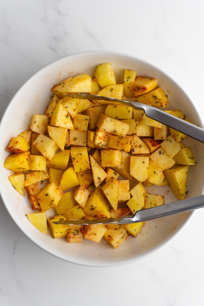 Diced potatoes in a bowl with spices on them.