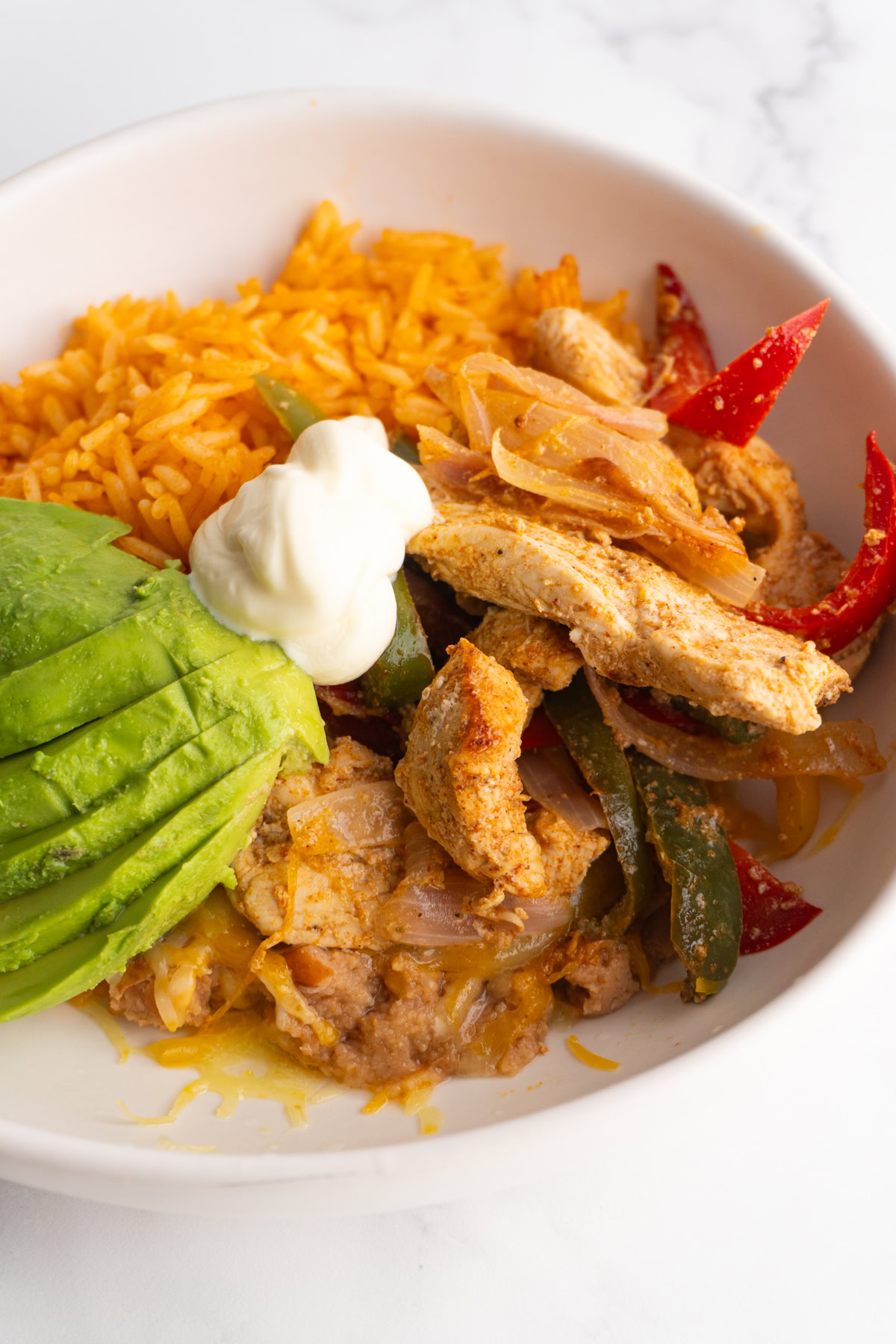 Chicken fajita bowl topped with sour cream and avocado.