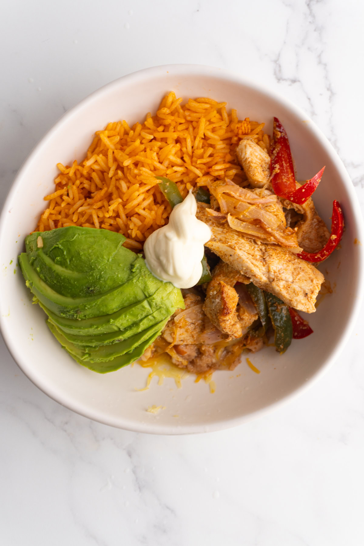 Overhead shot of a bowl with rice, chicken fajitas, avocado and sour cream.