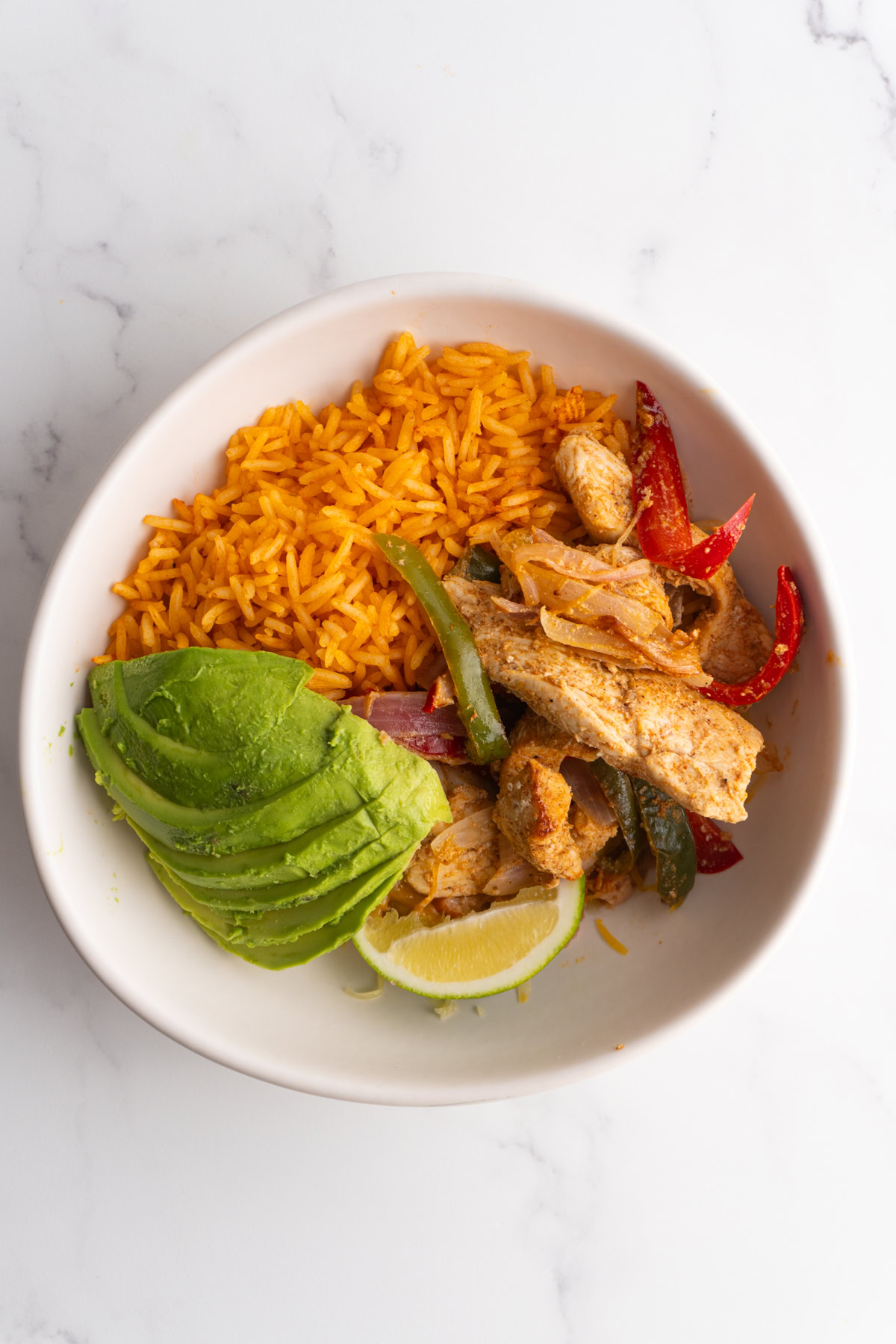 Overhead shot of a chicken fajita bowl with Mexican rice, chicken fajitas and avocado.