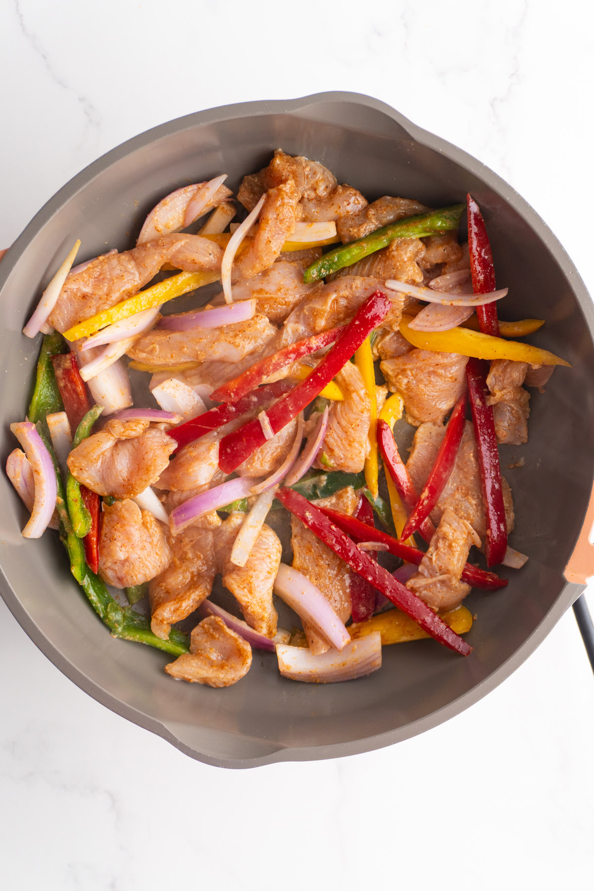 Seasoned chicken and veggies in a hot skillet.