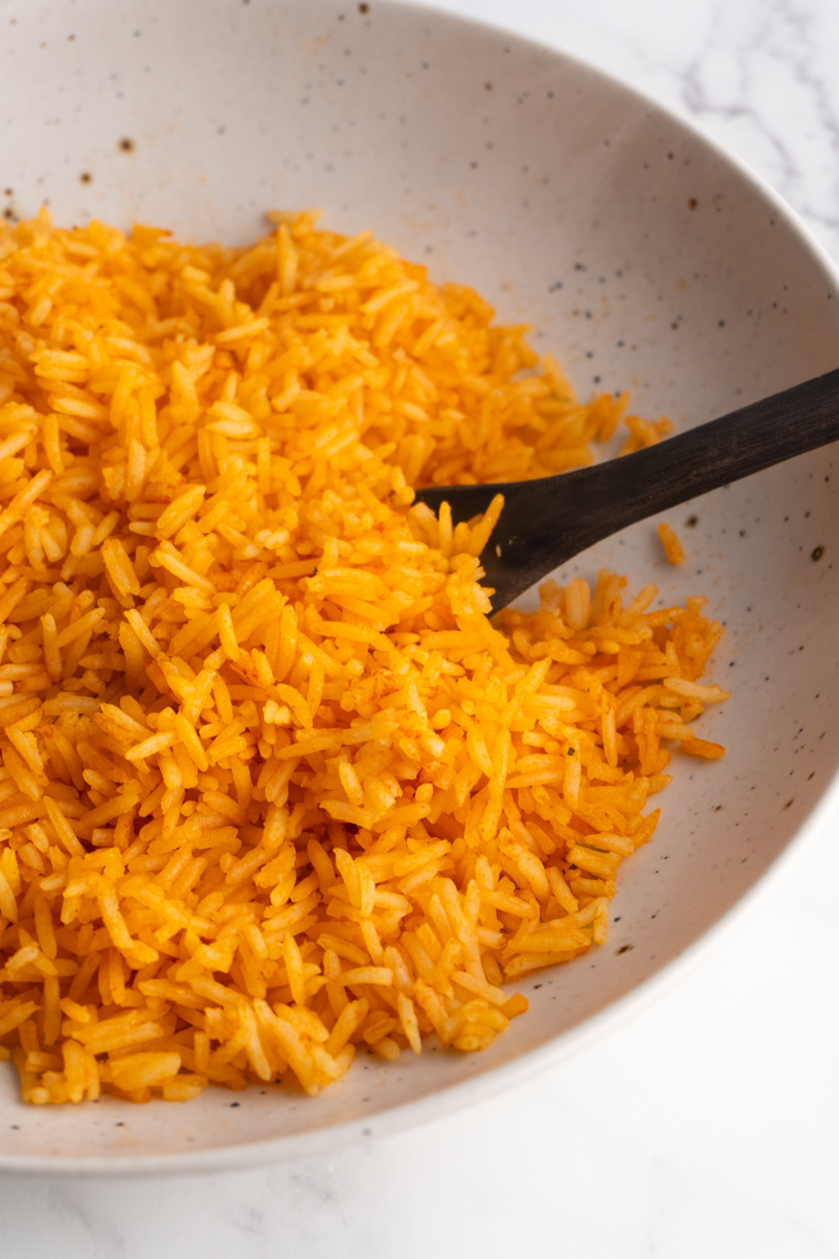 Side view of easy Spanish rice in a bowl with a wooden spoon.