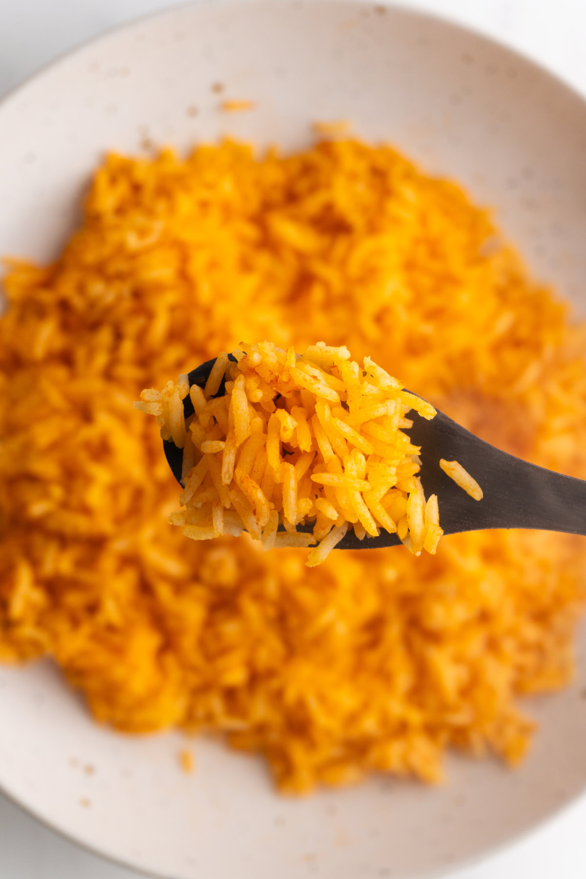 Mexican rice on a spoon hovering over the bowl of rice.