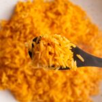 Overhead shot of rice on a wooden spoon with more rice underneath it in a bowl.