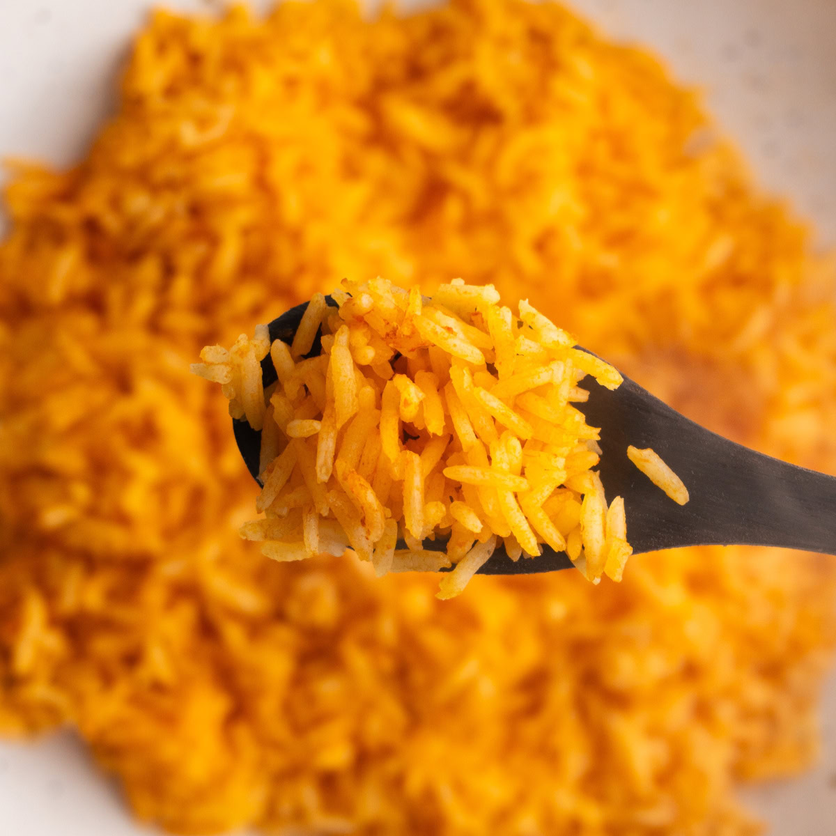 Overhead shot of rice on a wooden spoon with more rice underneath it in a bowl.