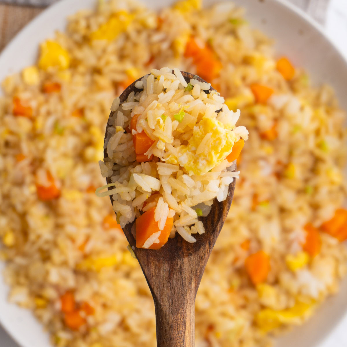 Close up of fried rice on a wooden spoon with more rice underneath it.