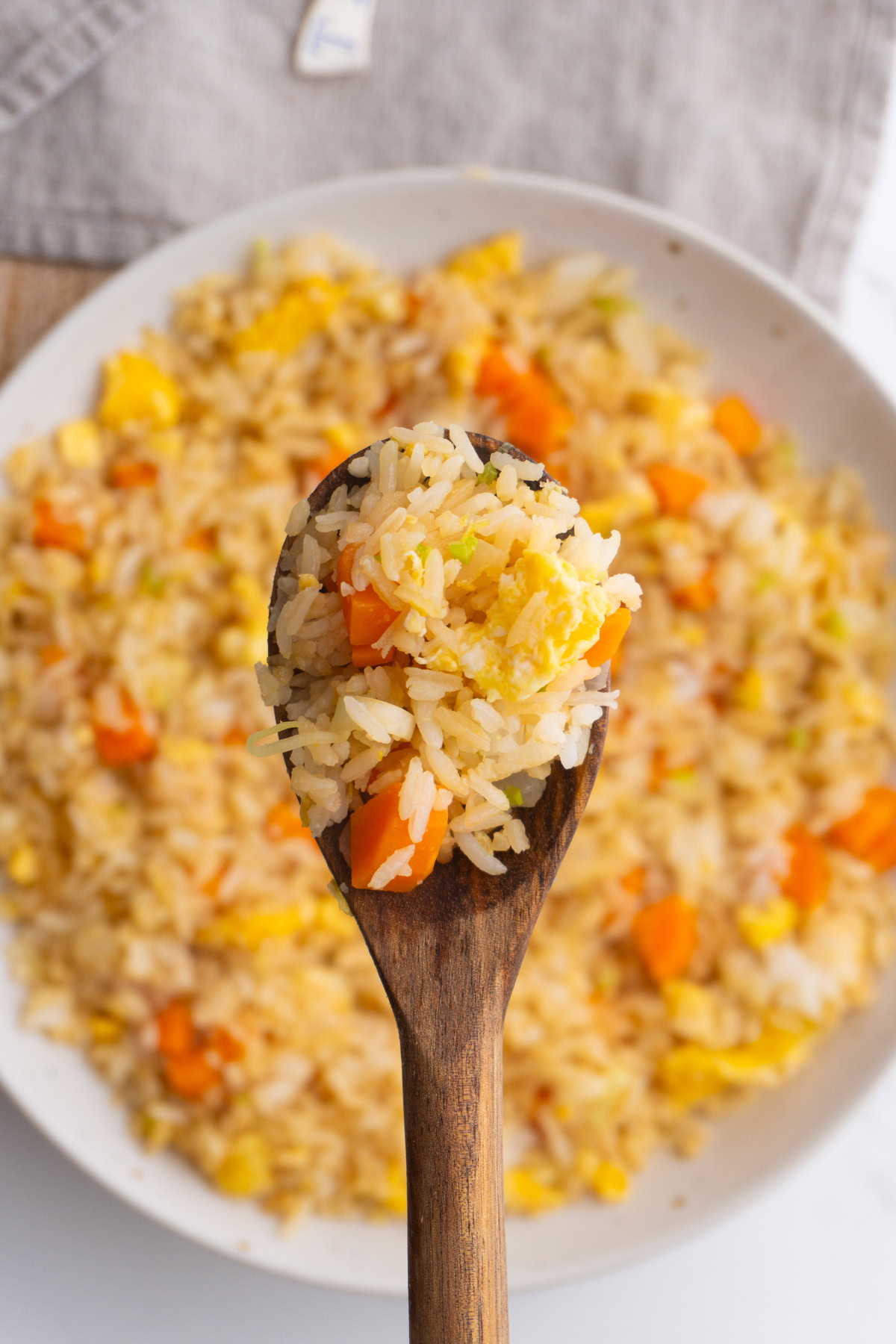 Wooden spoon with hibachi fried rice on it hovering over a bowl of fried rice.