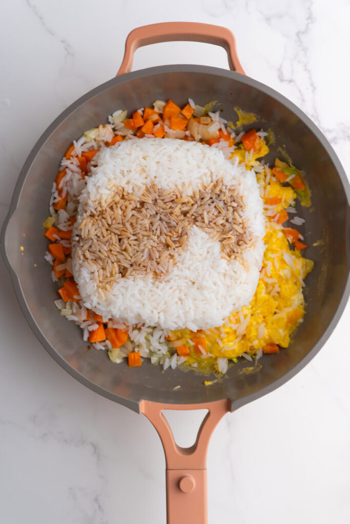 Soy sauce added to the rice, eggs, and veggies in a skillet.