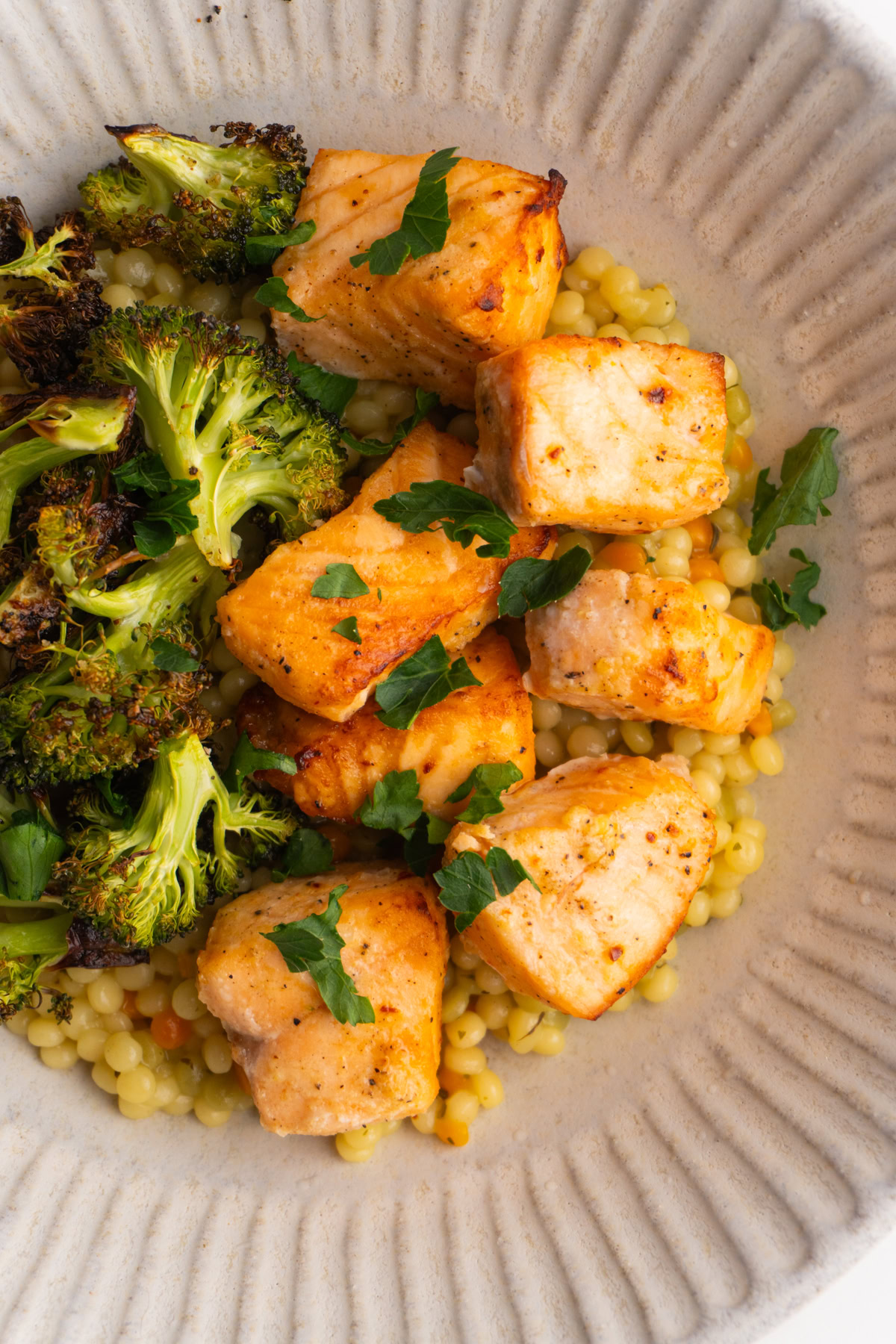 Overhead shot of salmon bites served on a bed of couscous with broccoli on the side.