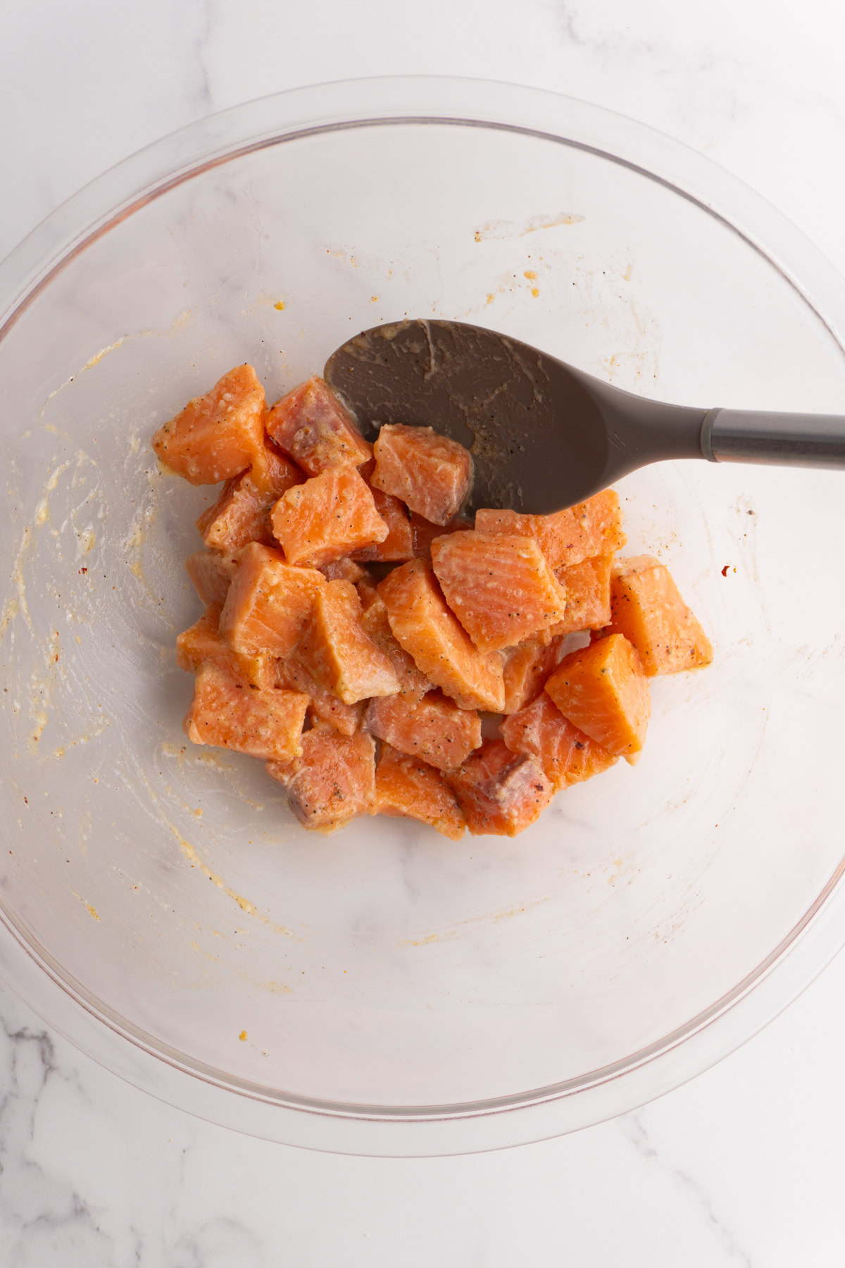 Chunks of salmon coating in seasoning in a mixing bowl.