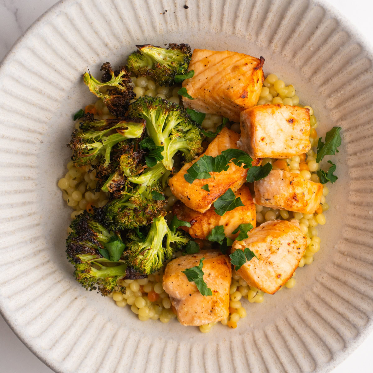Overhead shot of salmon couscous bowl with broccoli and parsley.