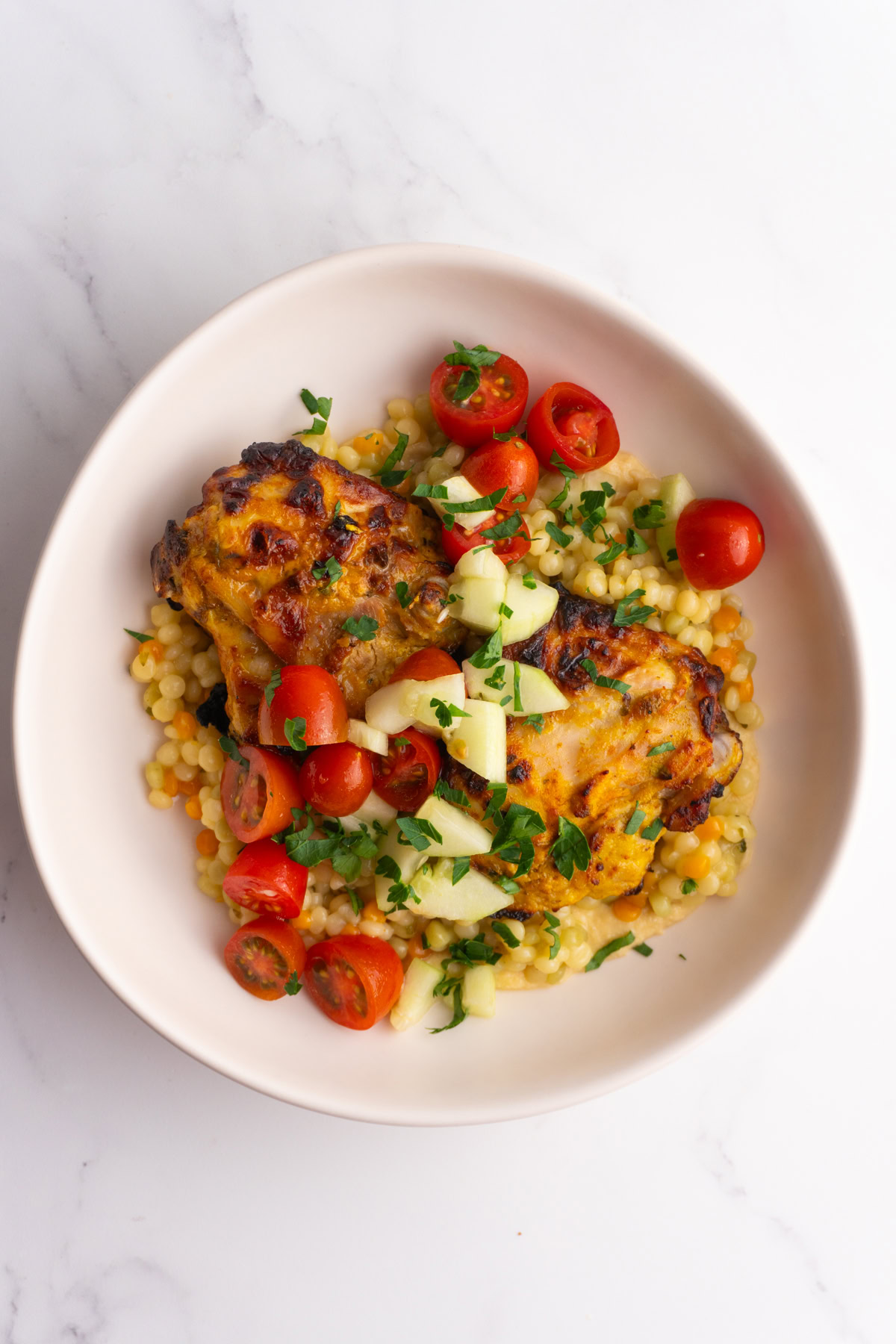 Overhead shot of a shawarma hummus couscous bowl garnished with parsley.