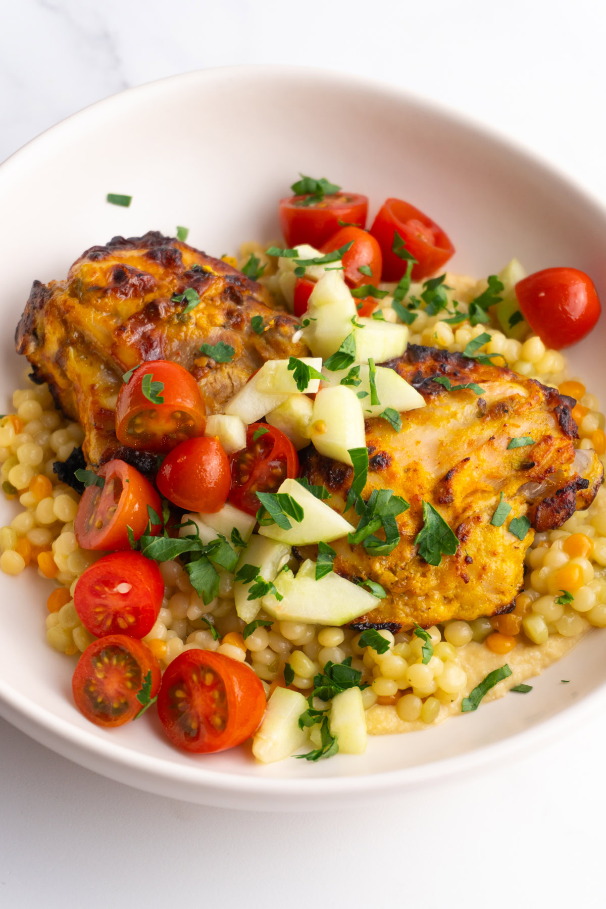 Side view of shawarma hummus couscous bowls with tomato and cucumber salad.