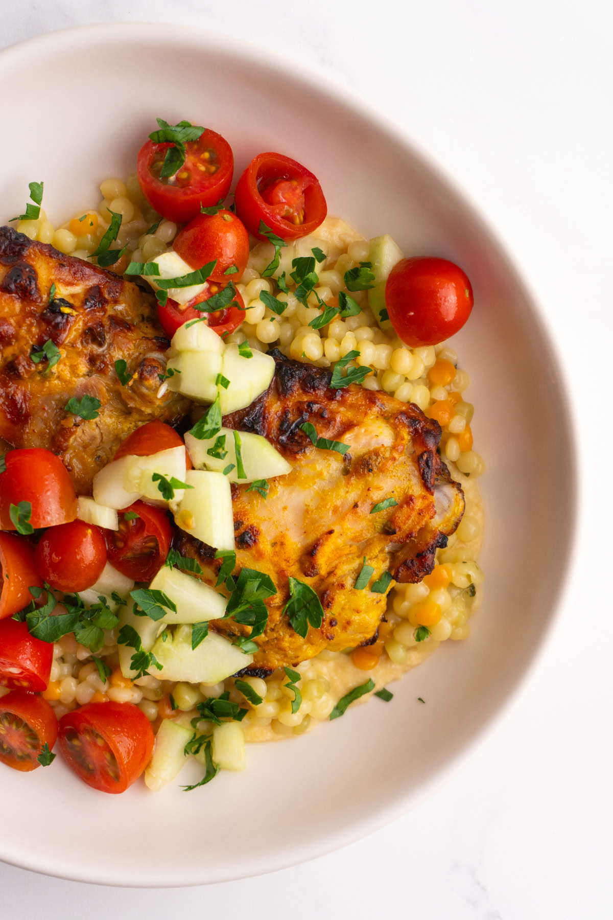 Half of the bowl served with hummus, couscous, chicken and tomato and cucumbers.