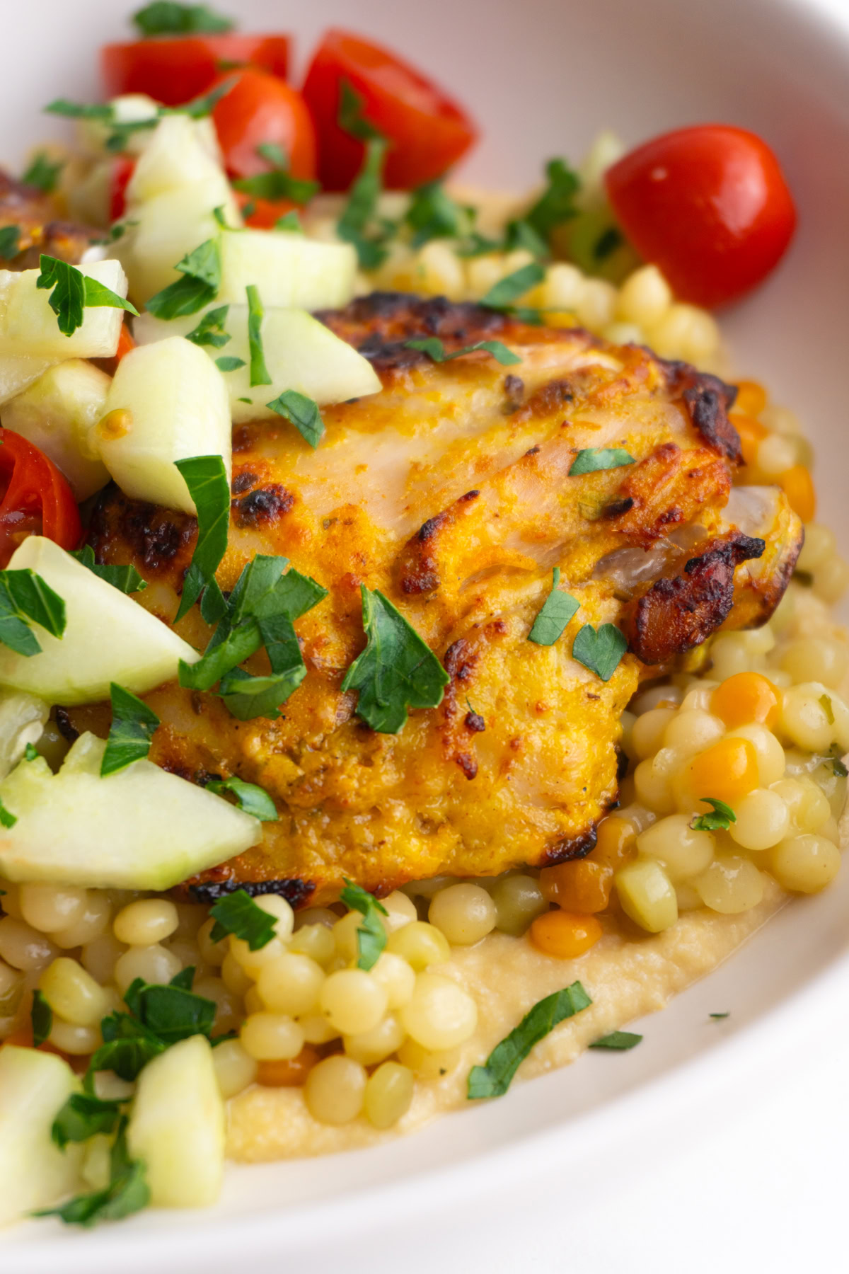 Side view close up of chicken on a bed of humus and couscous in a bowl.