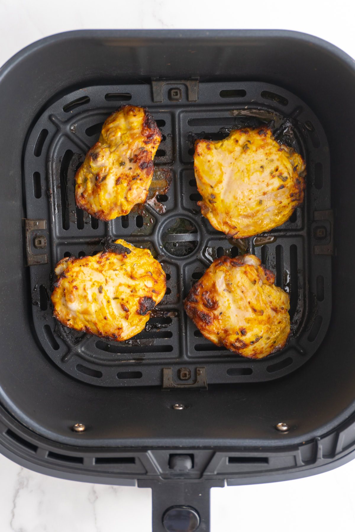 Chicken thighs in an air fryer basket after cooking.