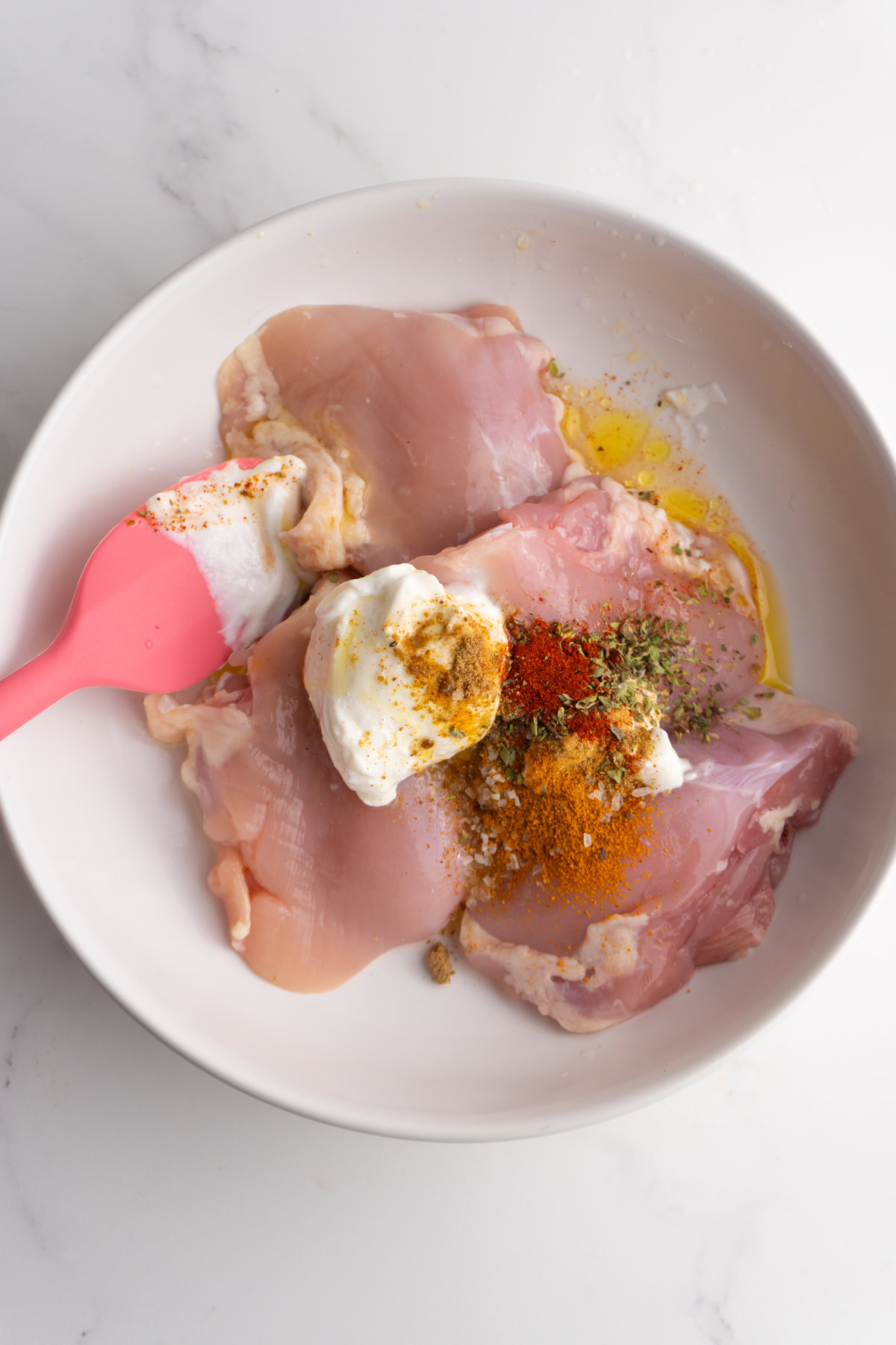Chicken thighs in a bowl with yogurt, olive oil and spices on top.