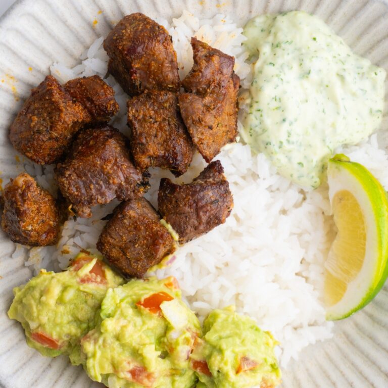 Bowl served rice, steak, cilantro sauce, guacamole and a lime wedge.