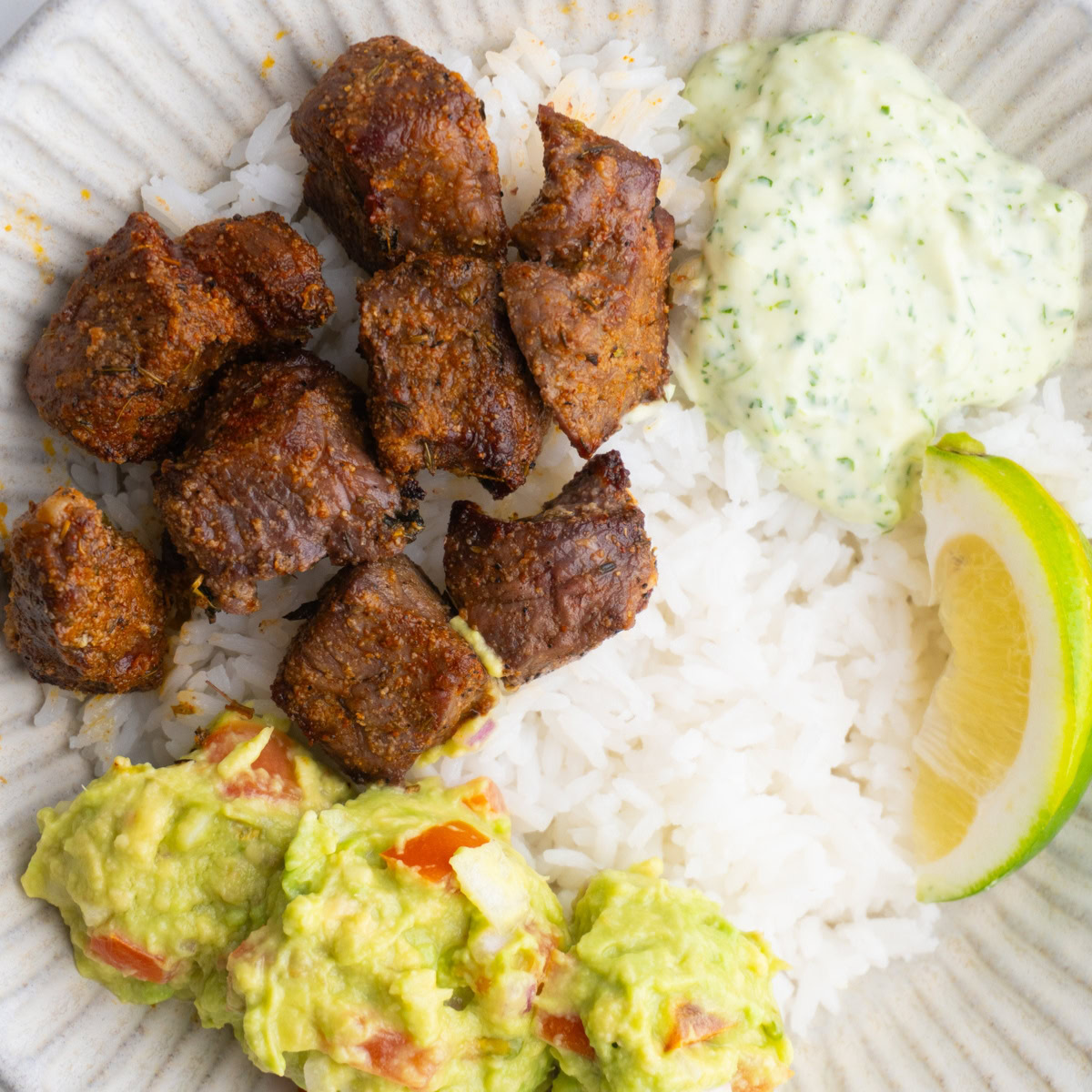 Bowl served rice, steak, cilantro sauce, guacamole and a lime wedge.