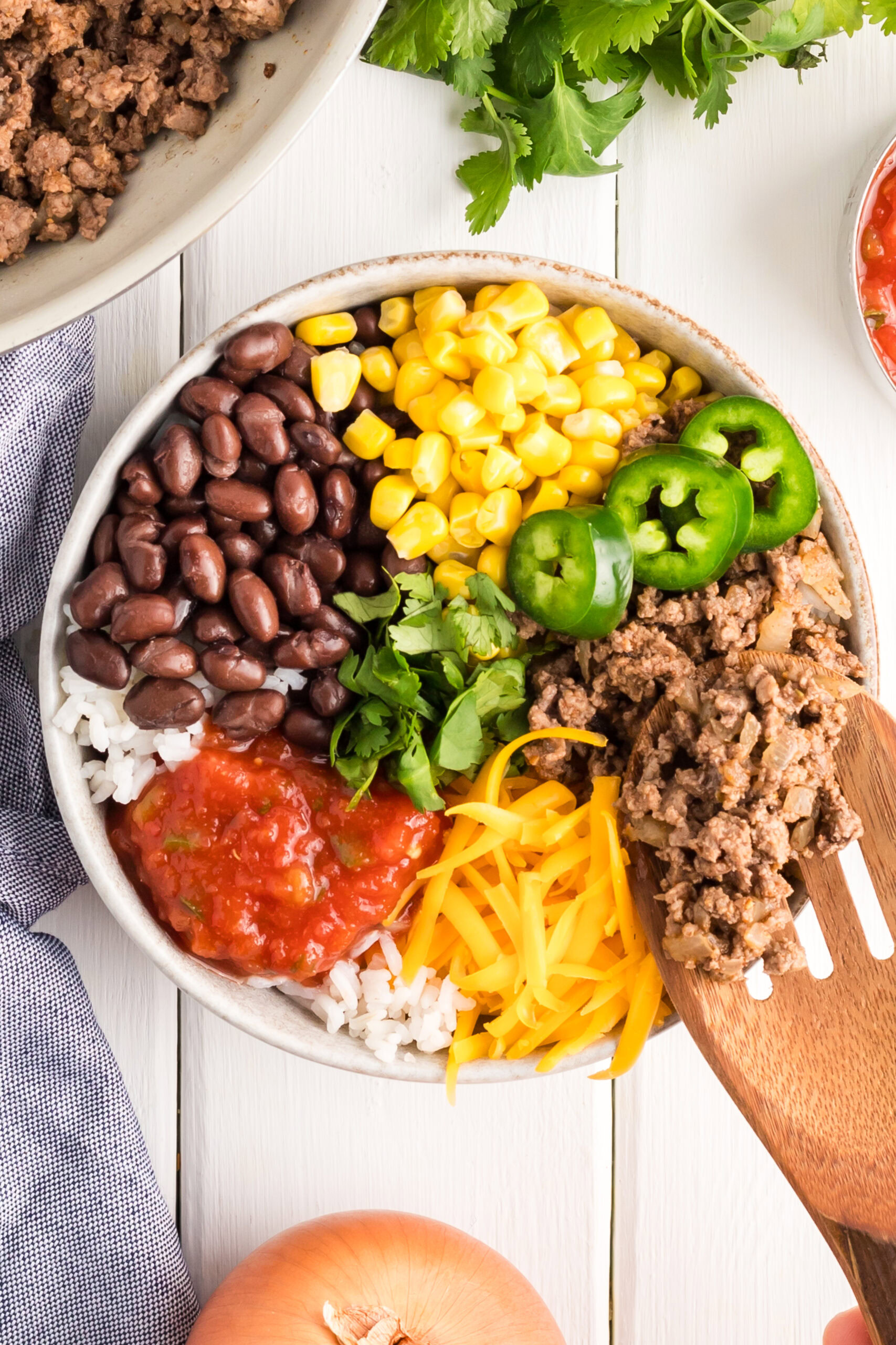 Wooden spoon placing ground chicken in the taco bowl.