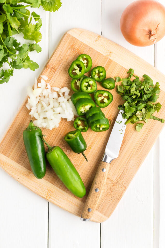 Sliced jalapeño, onion and cilantro on a wooden cutting board.
