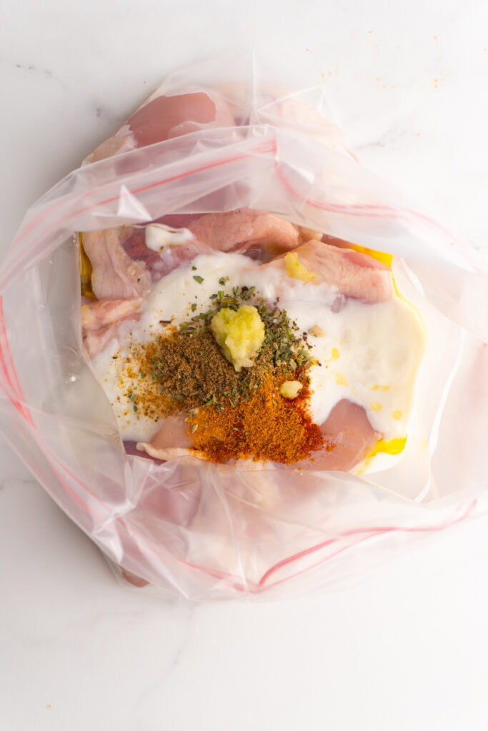 Chicken shawarma marinade ingredient on top of chicken in a bag.
