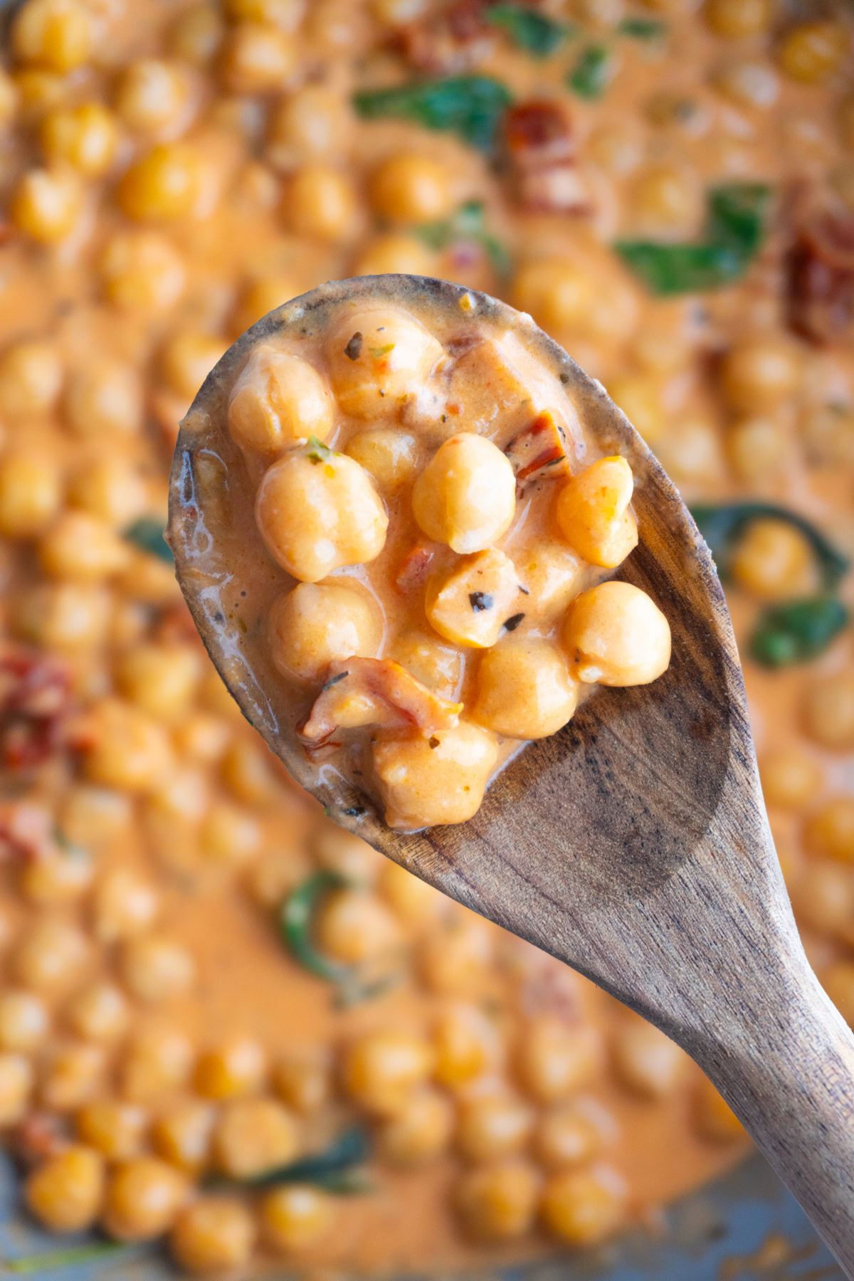 Wooden spoon of marry me chickpeas hovering over a skillet of them.