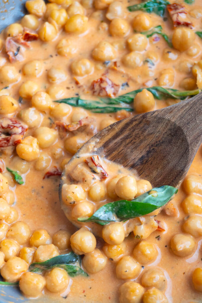 Marry me chickpeas in a skillet with a wooden spoon with some on it.