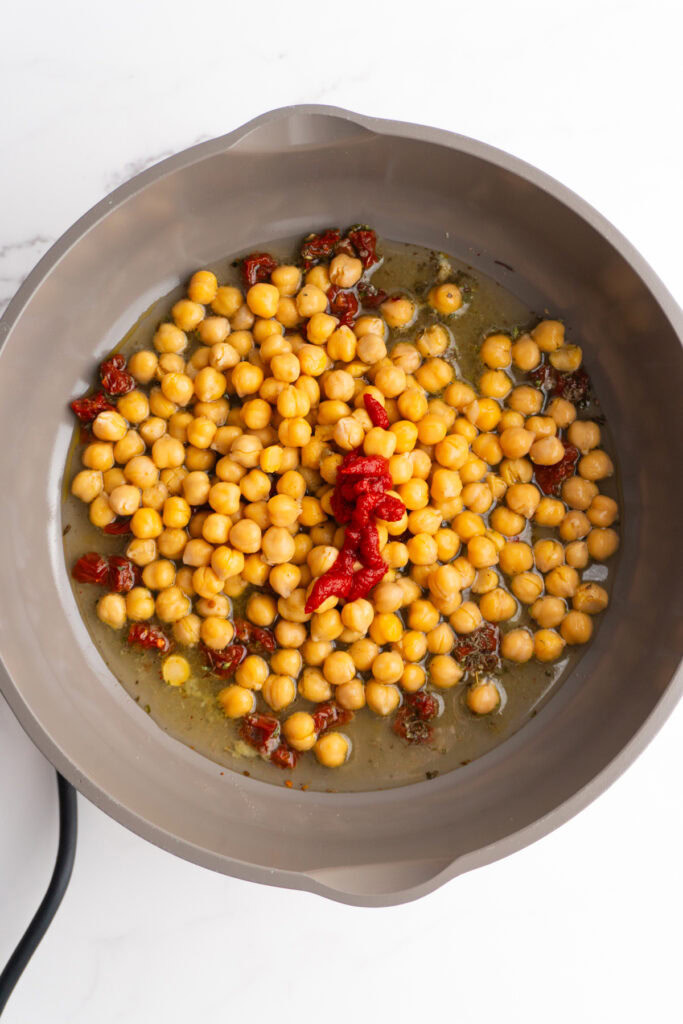 Chickpeas, tomato paste, and broth added to the skillet.
