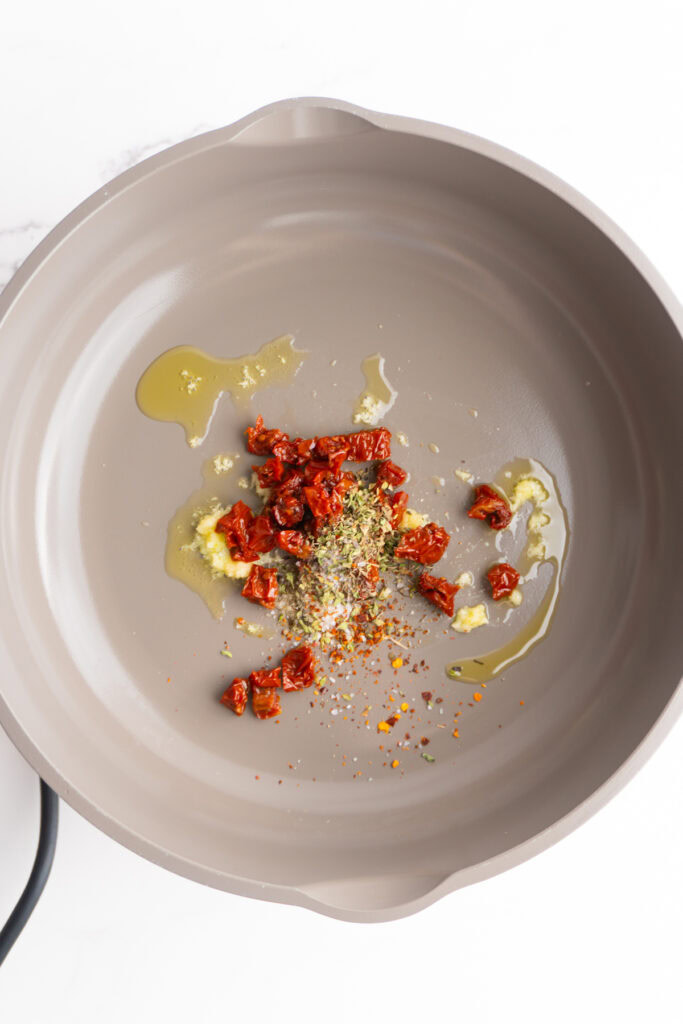 Olive oil, garlic, sun dried tomatoes, and spices in a skillet.