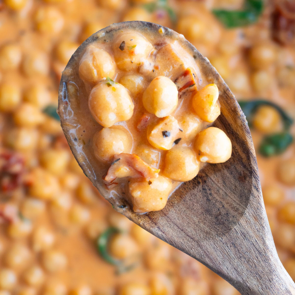 Wooden spoon of marry me chickpeas hovering over a skillet of them.