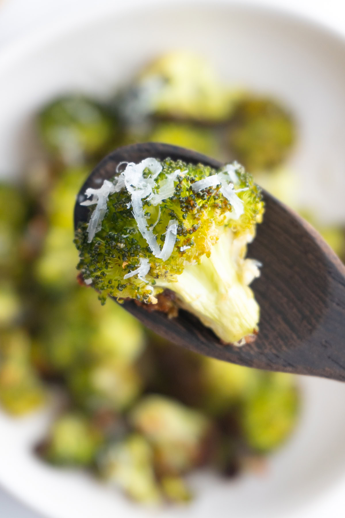 Close up of a piece of parmesan broccoli on a wooden spoon.