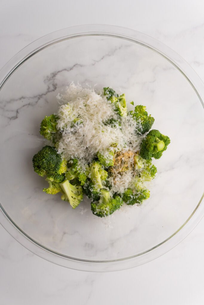 Broccoli florets in a bowl with spices and freshly grated parmesan.