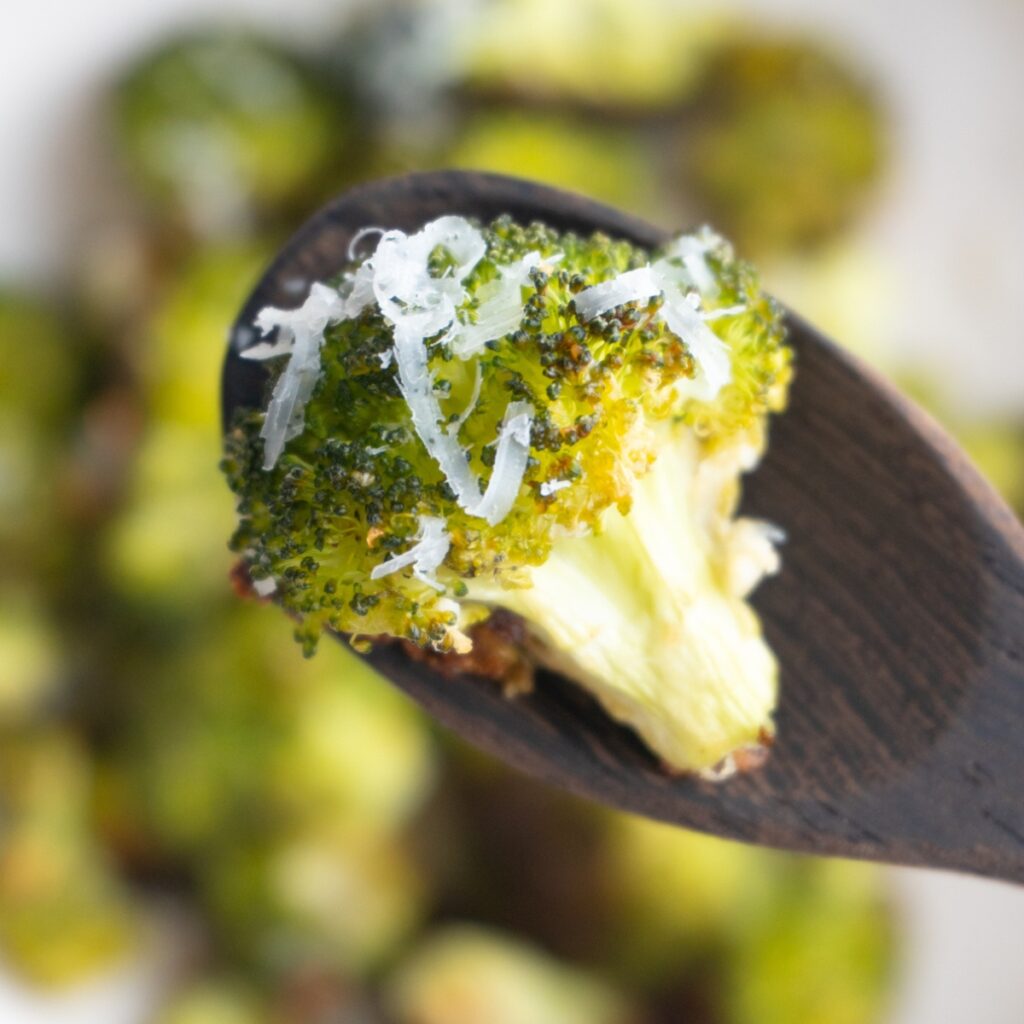 Parmesan roasted broccoli on a wooden spoon with more broccoli underneath.