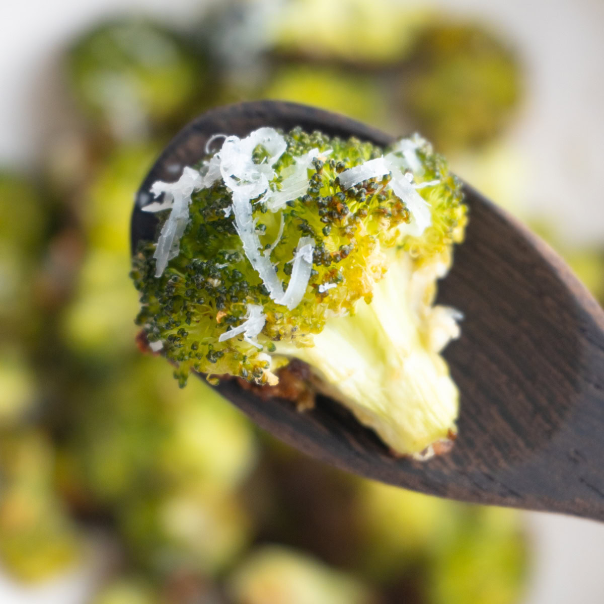 Parmesan roasted broccoli on a wooden spoon with more broccoli underneath.