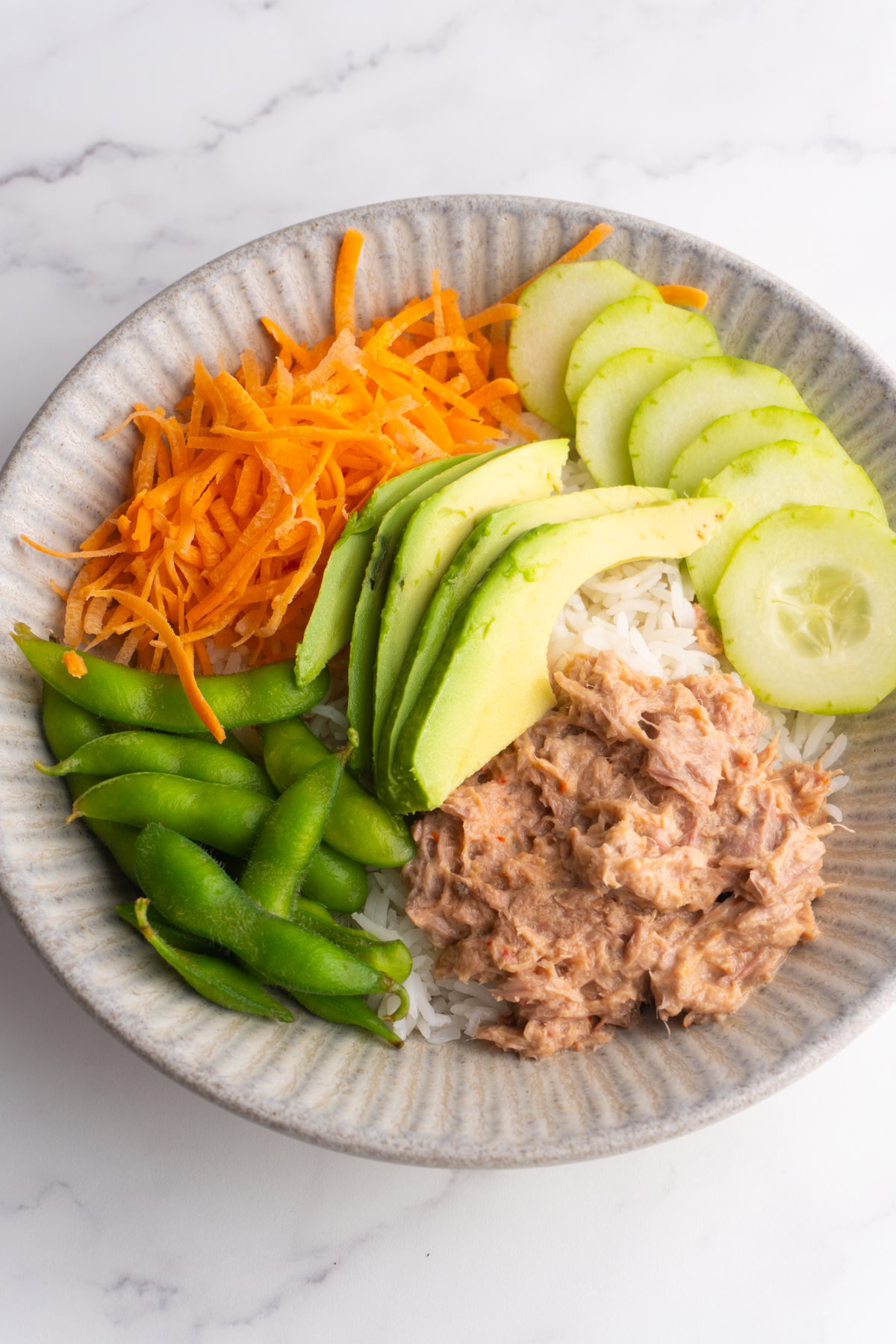 Spicy tuna bowls with rice, carrots, cucumber, avocado and edamame.