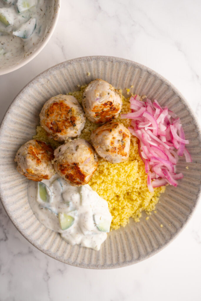 Overhead shot of a Mediterranean turkey meatball bowl with tzatziki and red onions.
