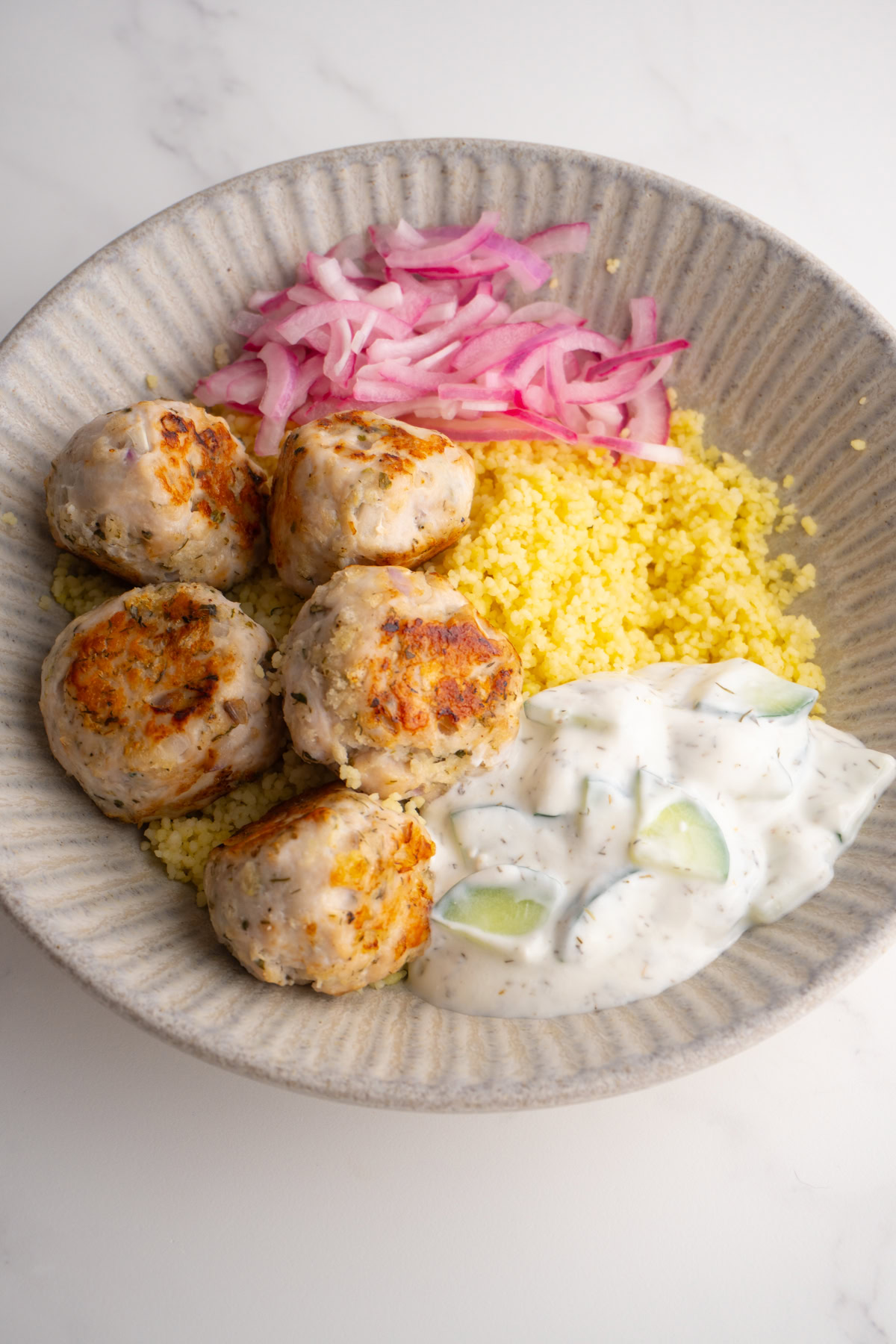Side view of a Mediterranean meatball bowl with couscous and tzatziki sauce.
