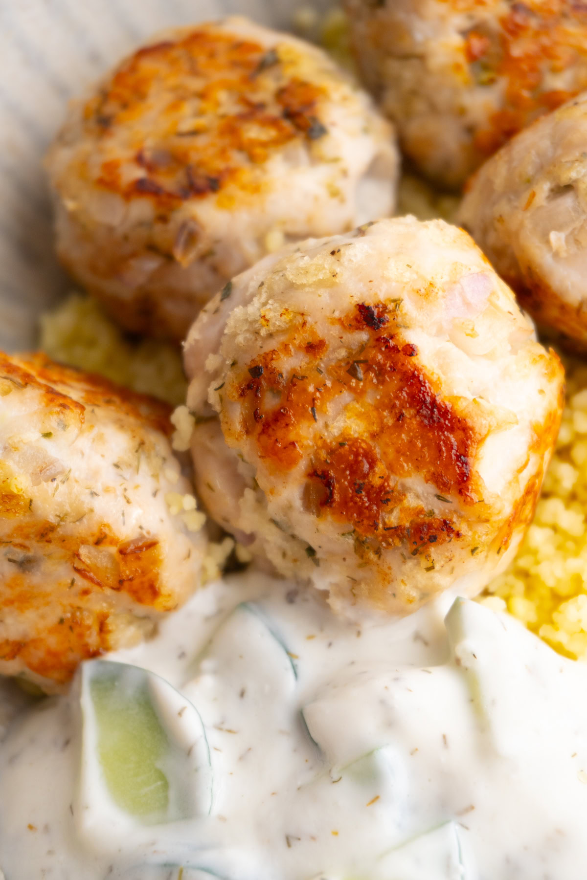 Greek turkey meatballs next to tzatziki sauce on a bed of couscous.