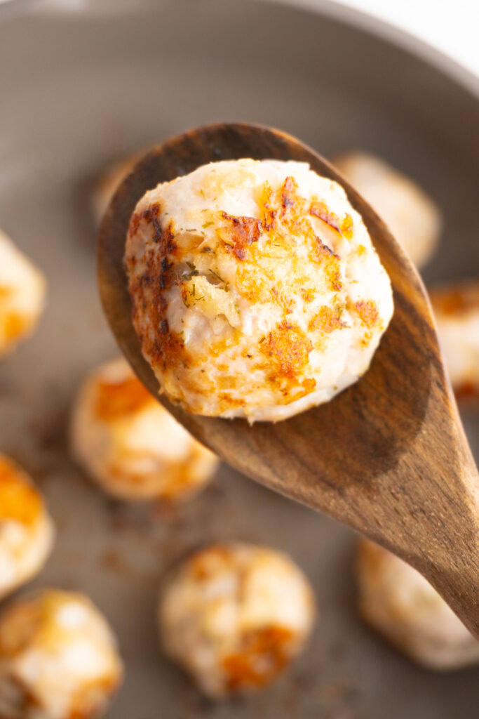 Close up of a Greek turkey meatball on a wooden spoon hovering over the skillet.