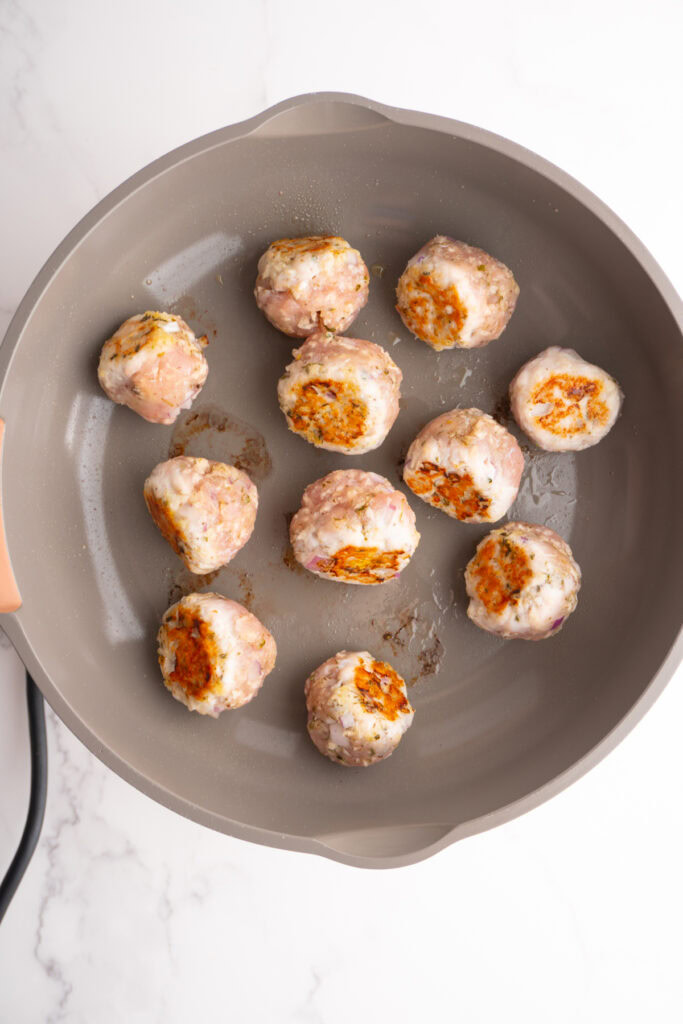 Greek turkey meatballs in a skillet being flipped around to sear on their sides.
