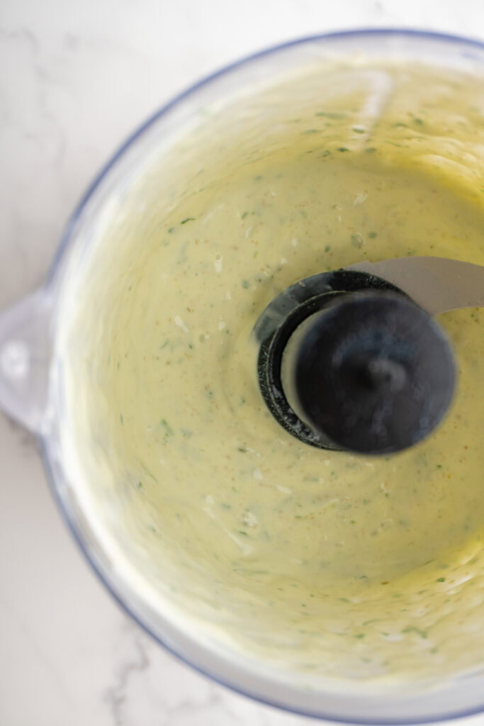 Close up of green goddess dip in the food processor after being blended.