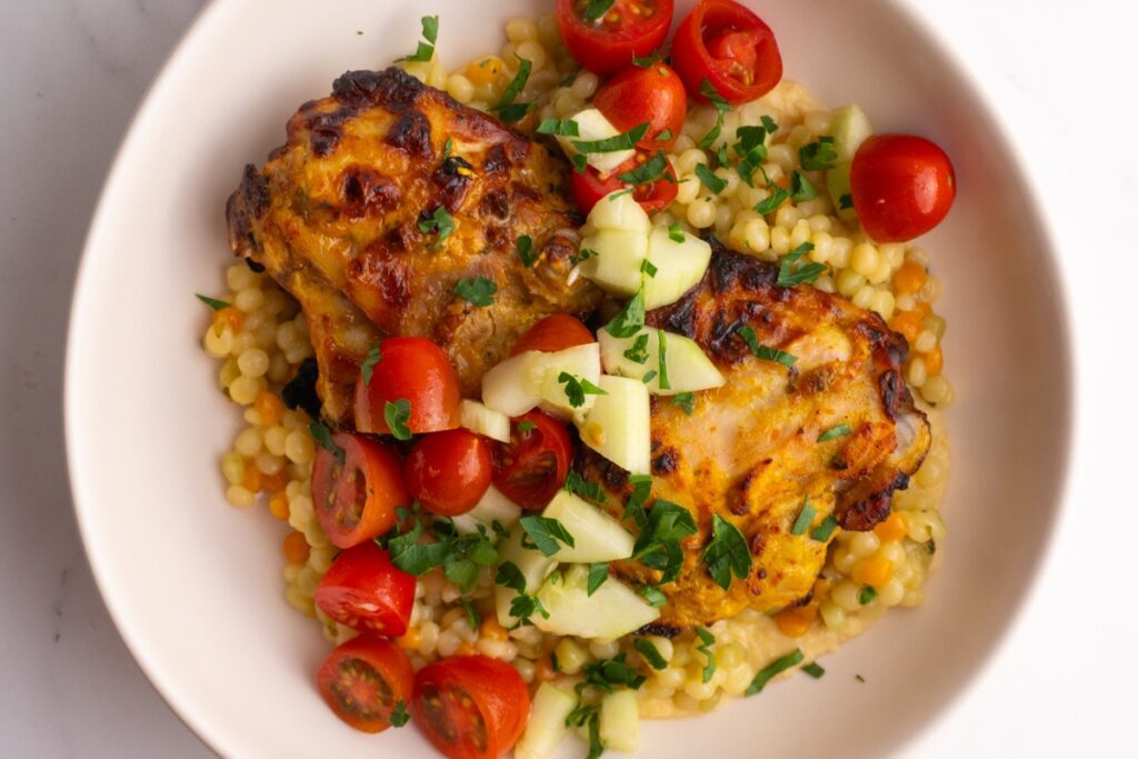 Overhead shot of a chicken hummus bowl with a cucumber tomato salad on top.