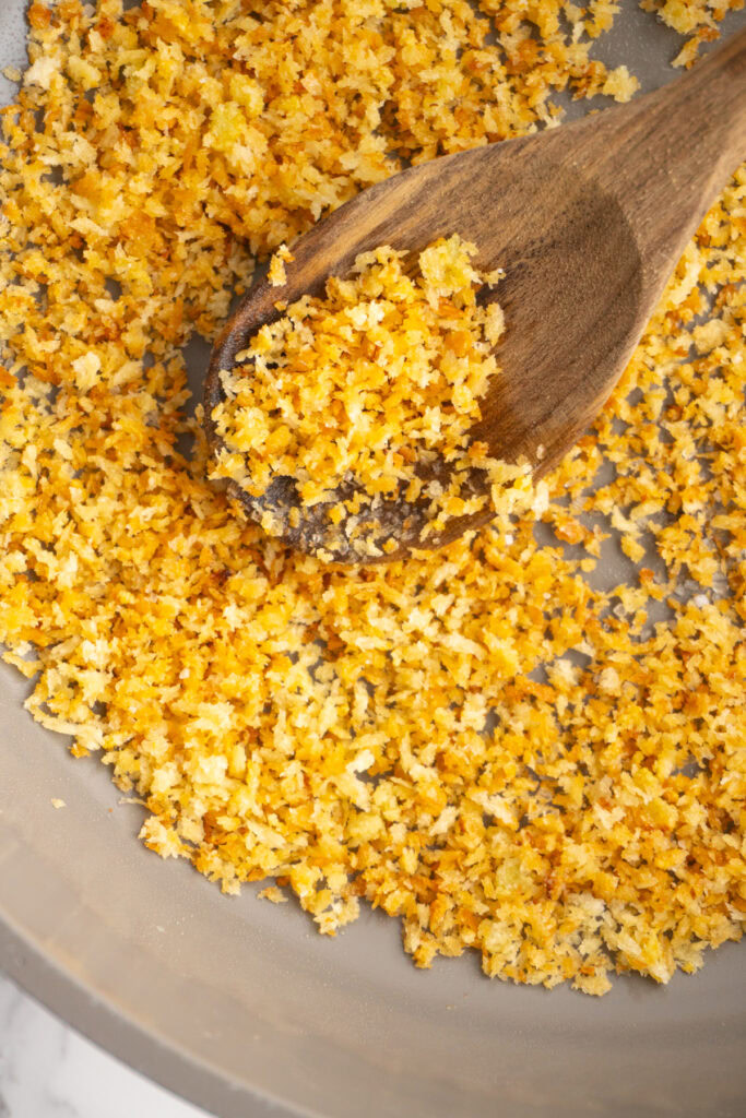 Garlic breadcrumbs in a skillet with a wooden spoon.
