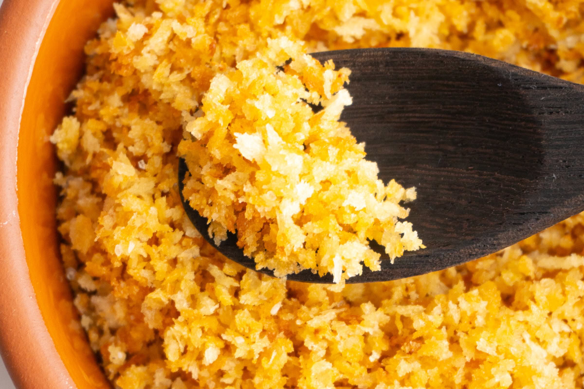 Close up of garlic breadcrumbs with a wooden spoon scooping some up.