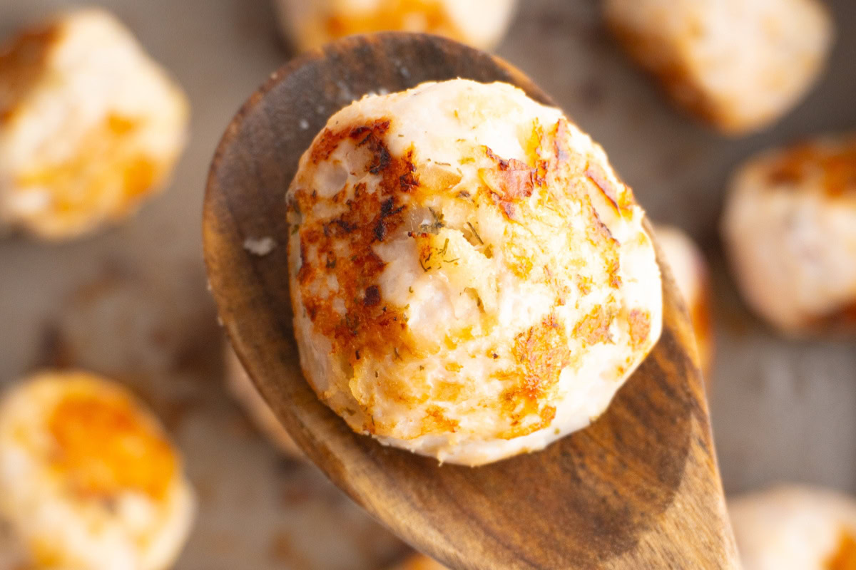 Greek turkey meatball on a wooden spoon with more meatballs in the background.